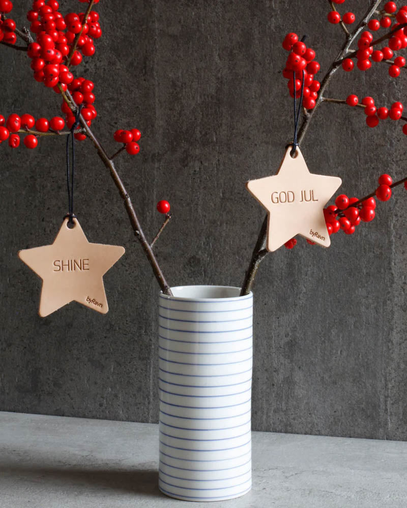 NORTH julestjerner i naturfarvet læder med graveringerne "Shine" og "God jul" hængt på grene med røde bær i stribet vase