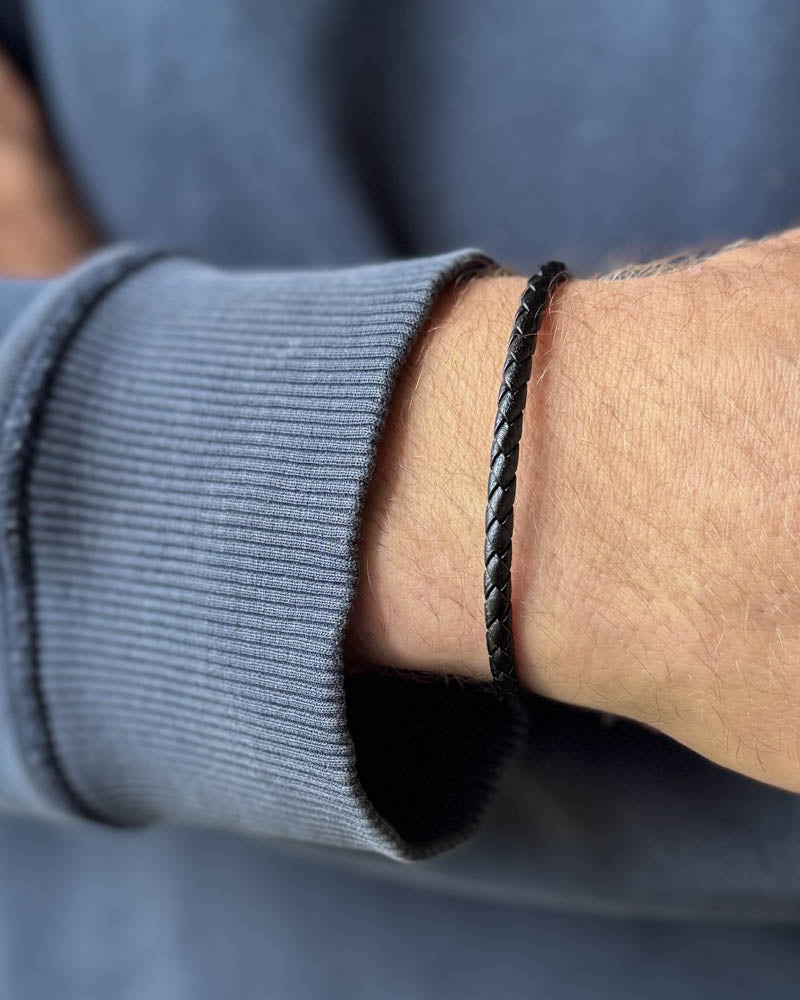 RIO læderarmbånd i sort flettet læder båret om mandehåndled, blågrå sweatshirt