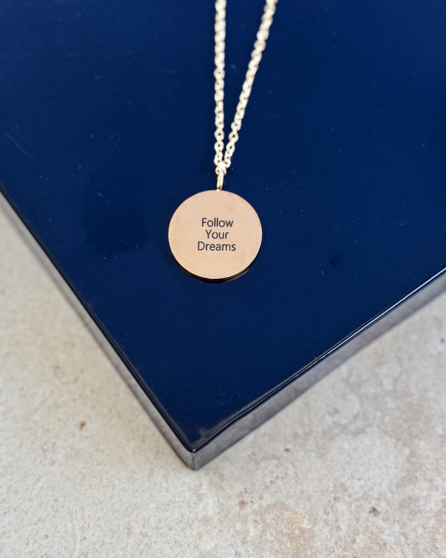 SIA QUOTE halskæde i guldbelagt stål med graveringen "Follow your dreams" på rundt vedhæng, på mørkeblå æske