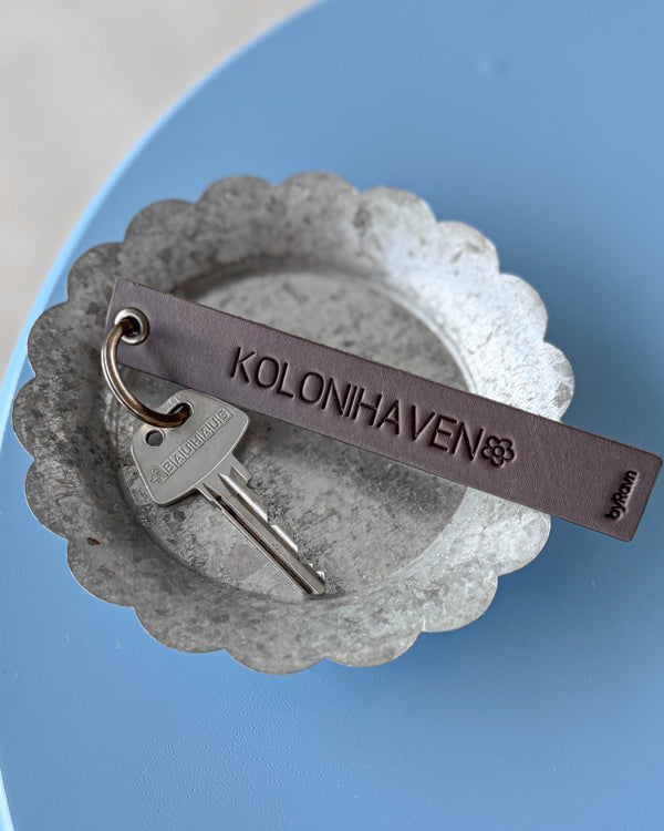 SOLO Large nøglering i mørkebrunt læder med graveringen "Kolonihaven" og blomst, med nøgle i zinkskål