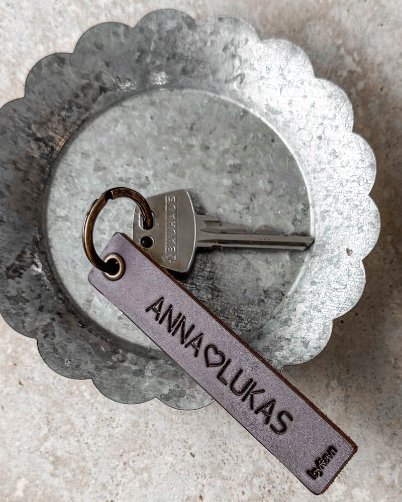 SOLO Medium nøglering i mørkebrunt læder med personlig gravering "Anna ♡ Lukas" og nøgle i zinkskål