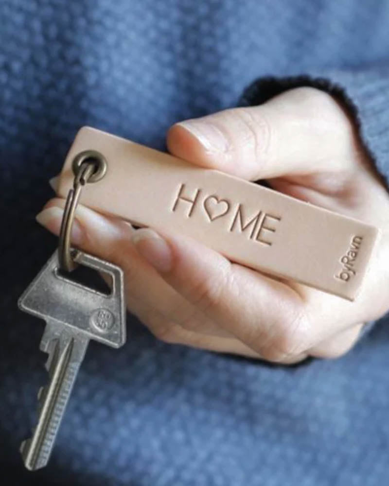 SOLO Small nøglering i naturfarvet læder holdt i hånden med nøgle og graveringen "Home" med hjerte som O