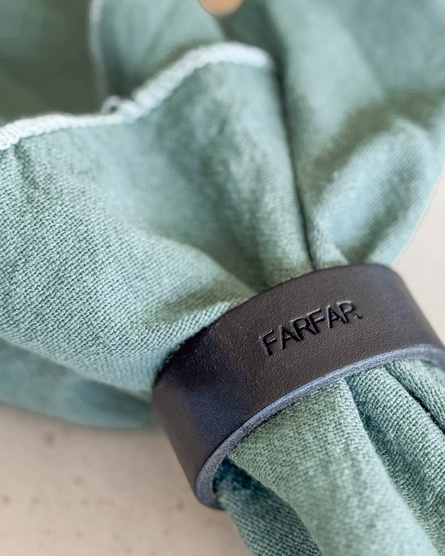 KNOT servietring bordkort i sort læder med graveringen "Farfar" om lysegrøn stofserviet