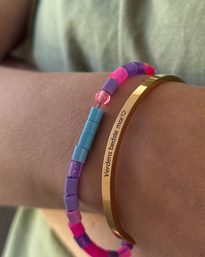 VENUS armbånd i guldbelagt stål med graveringen "Verdens bedste mor" ♡ båret sammen med farverigt perlearmbånd