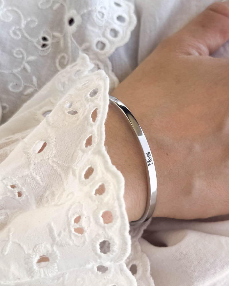 VENUS STICK armbånd i sølvfarvet rustfrit stål med tændstikfamilie graveret, båret til hvid bluse med broderi